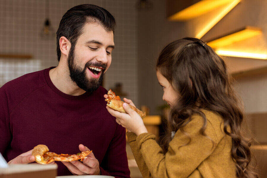 A daughter feeding her father a slice of pizza.
