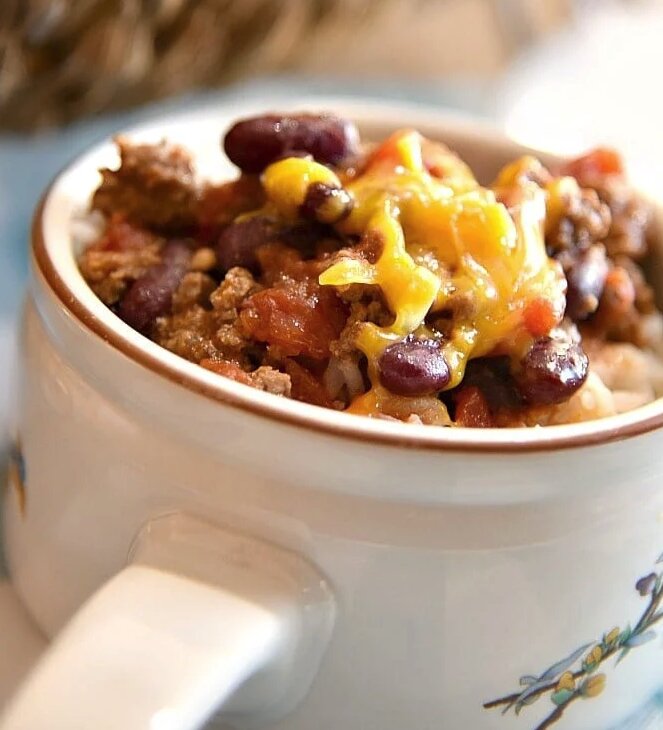 A mug filled with meat and beans chili and topped with cheese. 