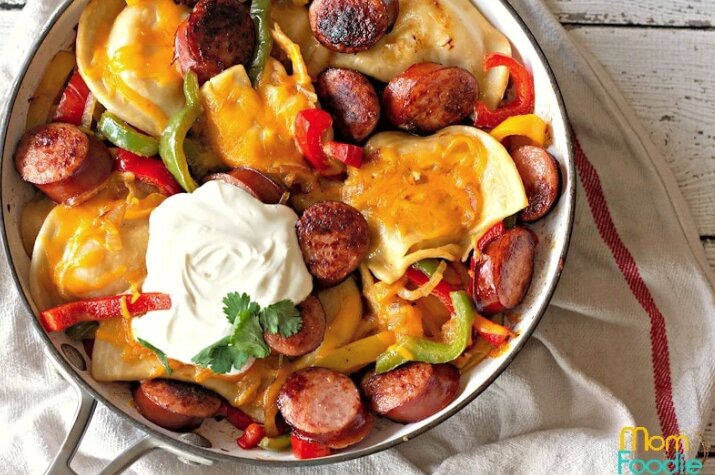A bowl filled with pierogis and kielbasa on a white tablecloth. 