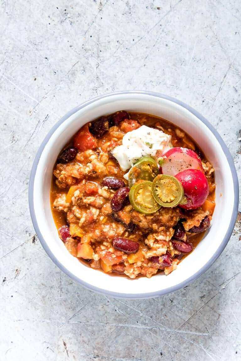 A white bowl filled with chili and a dollop of sour cream on top of a counter. 