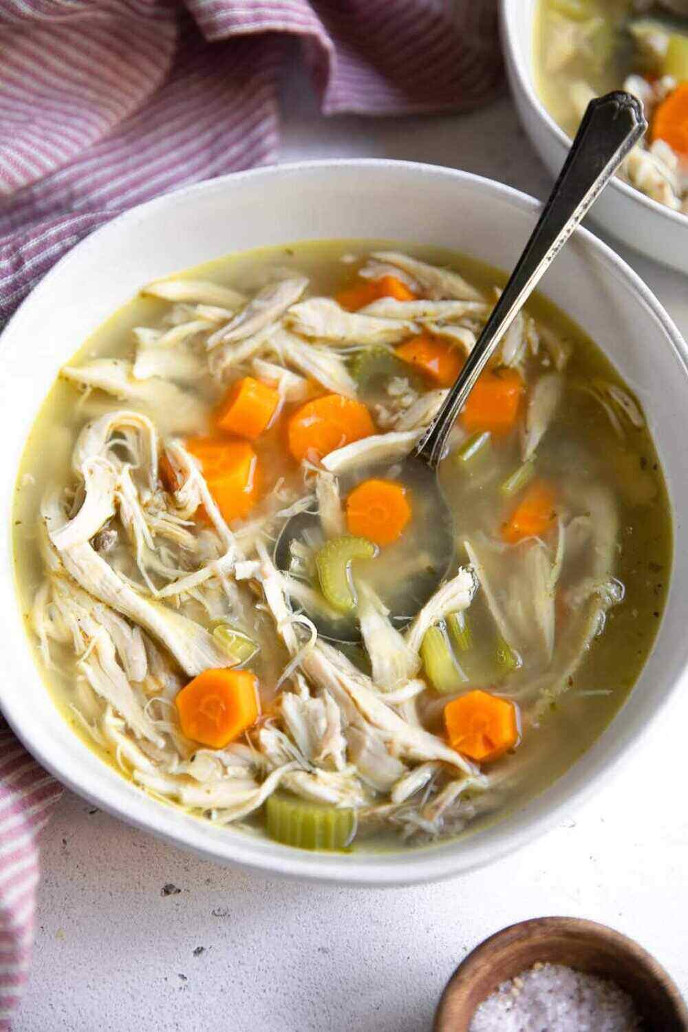 A bowl of hearty chicken, carrot and celery soup with a spoon in it. 