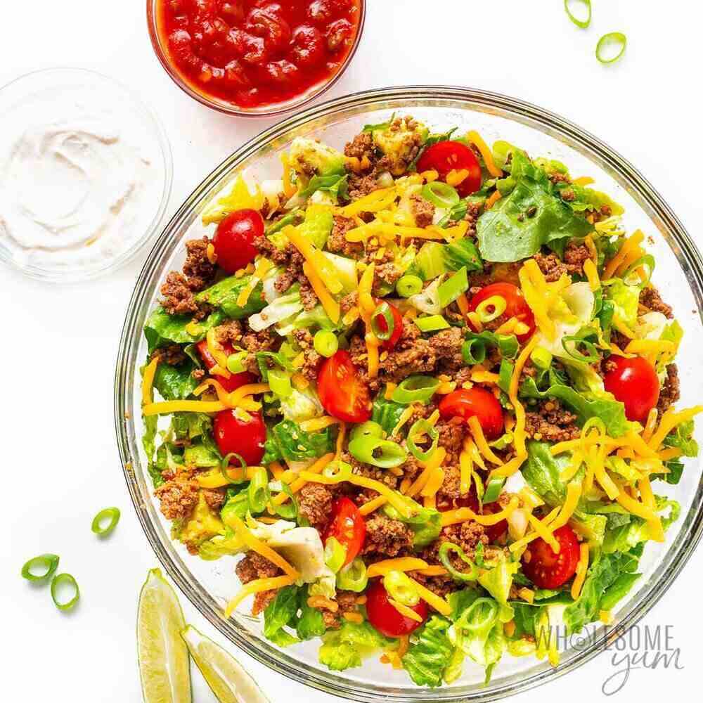 A counter top with a colorful bowl filled with salad, ground taco meat and tomatoes. 