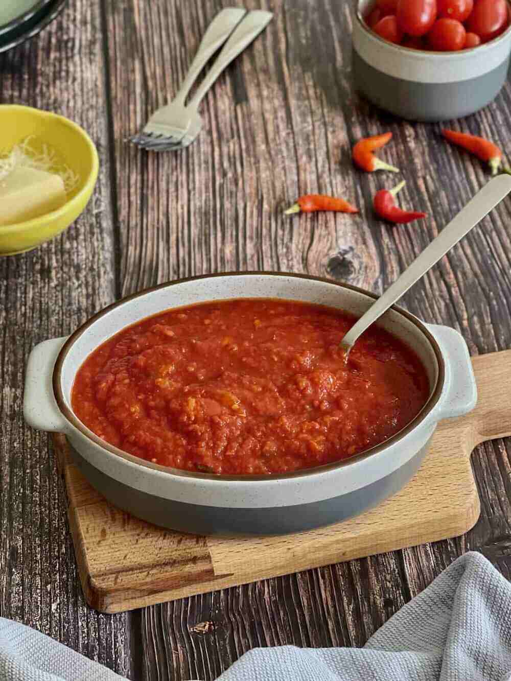 A bowl of delicious red homemade spaghetti sauce with a spoon in it on a wooden table.