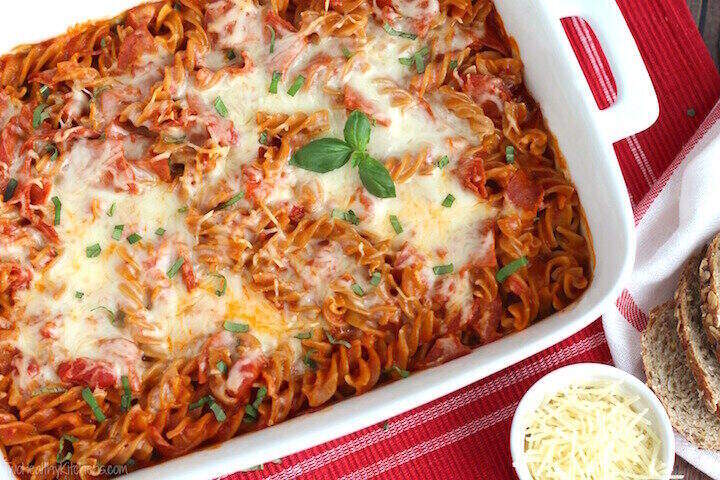 A red casserole dish filled with a cheesy, marinara based casserole. 