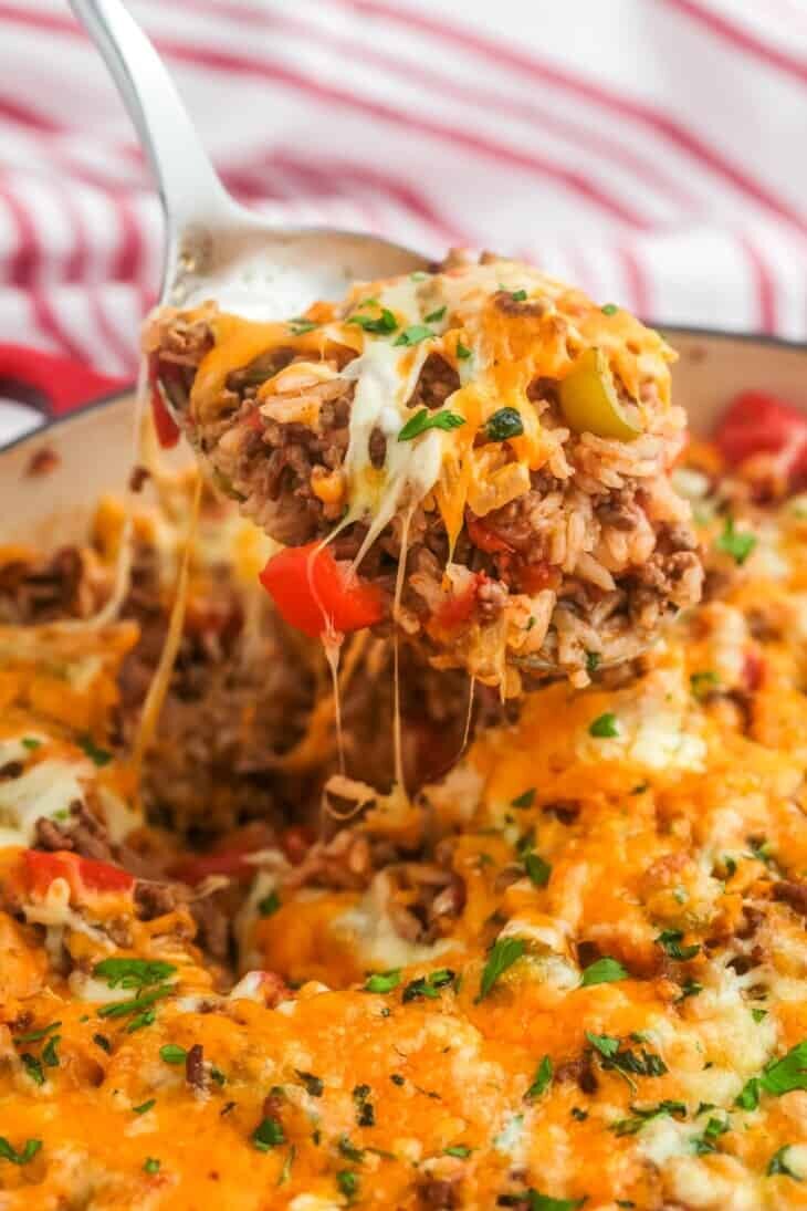 A striped table cloth lies beneath a plate with a hearty stuffed pepper casserole. A spoon is scooping up the casserole. 