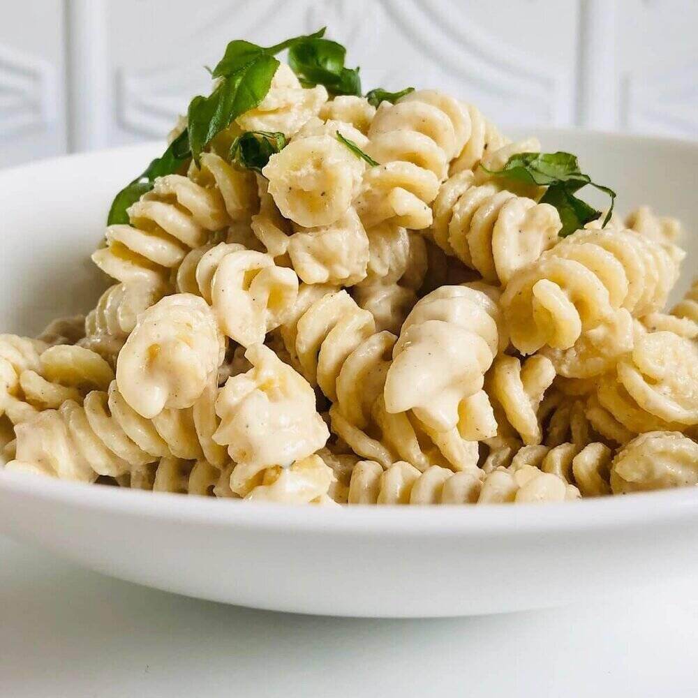 A white plate stacked high with corkscrew pasta and tahini sauce.