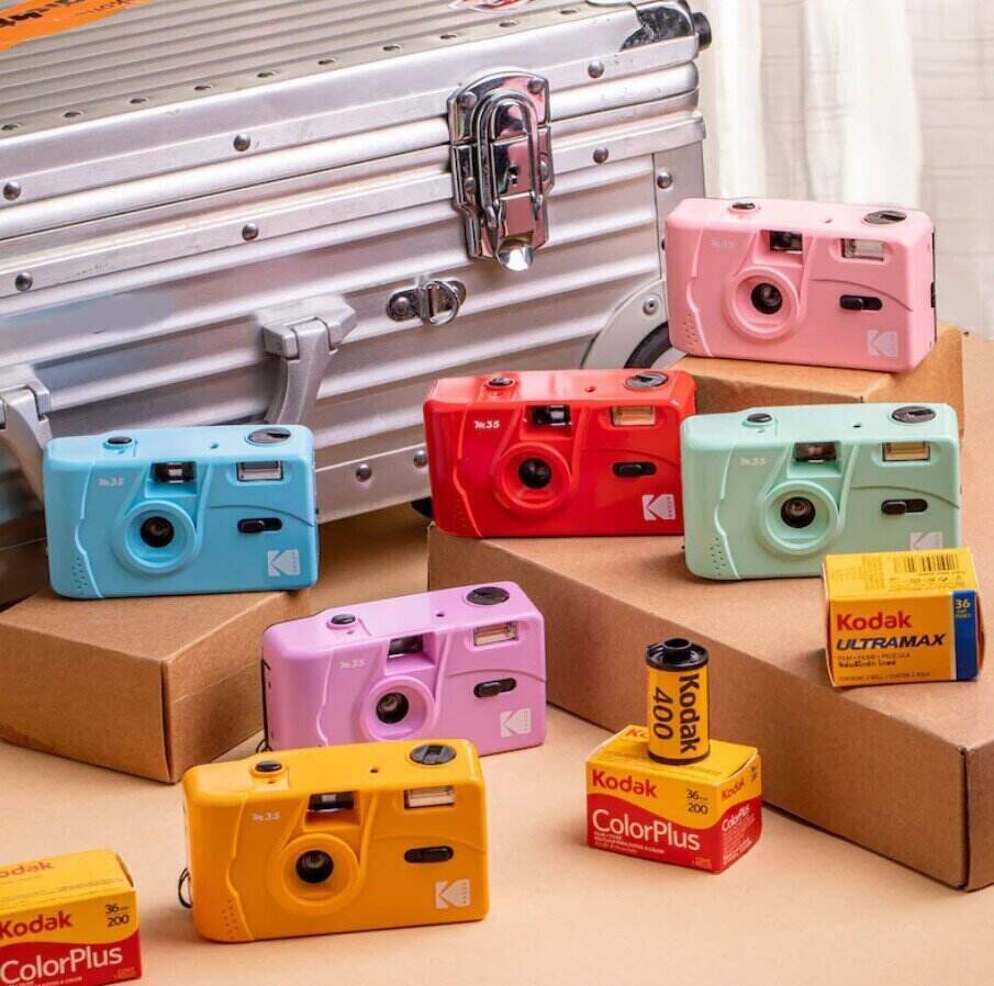 multiple pastel colored disposable cameras sitting on boxes on a table with rolls of photo film