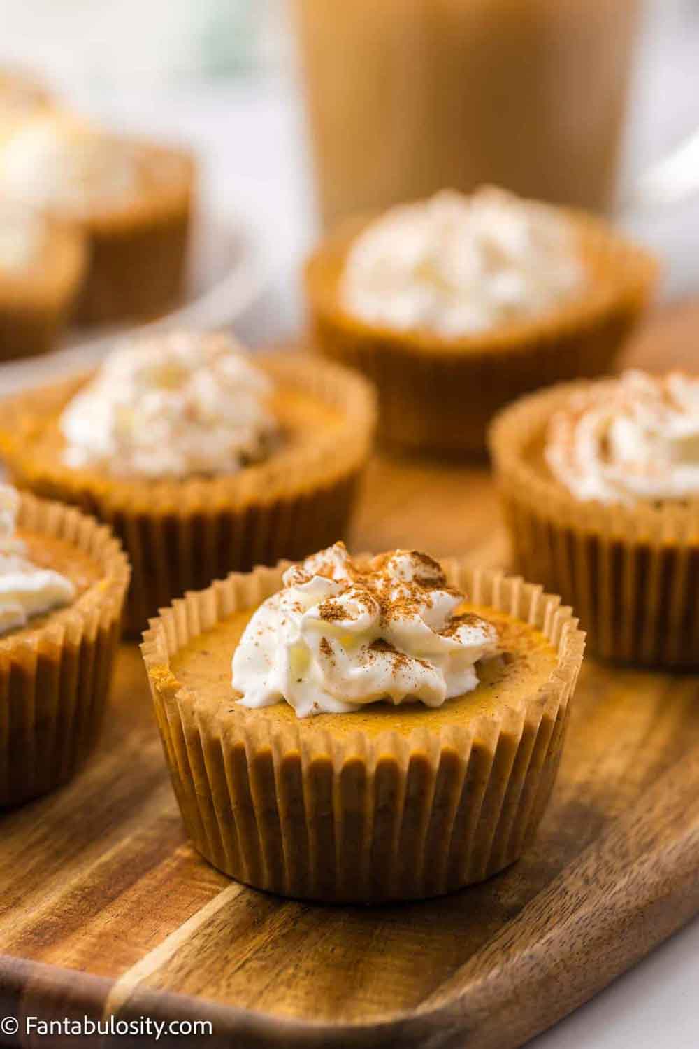 Pumpkin cheesecake bites on a plate, each topped with whipped cream.