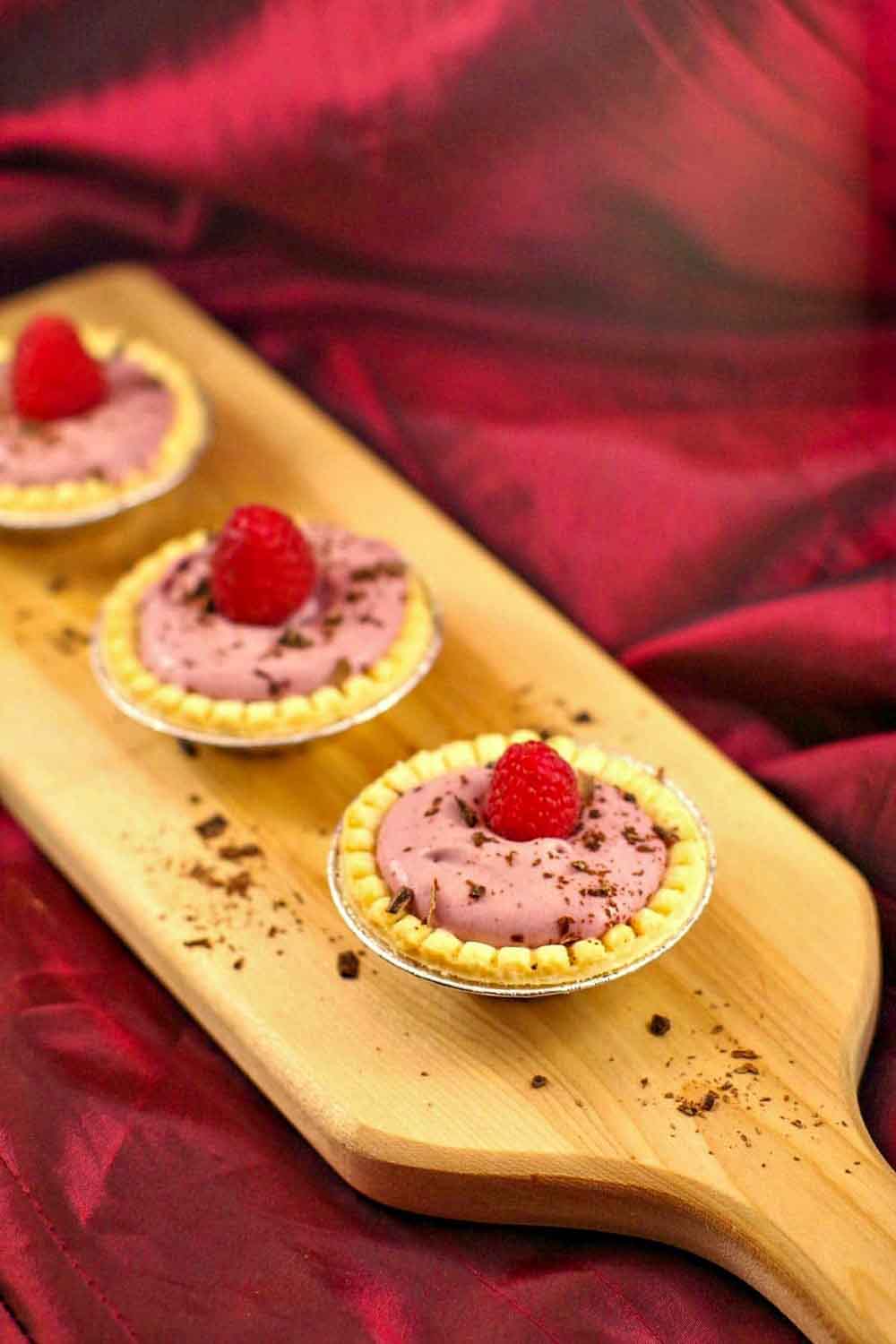 Mini tarts filled with raspberry tiramisu cream, topped with fresh raspberries and chocolate shavings.