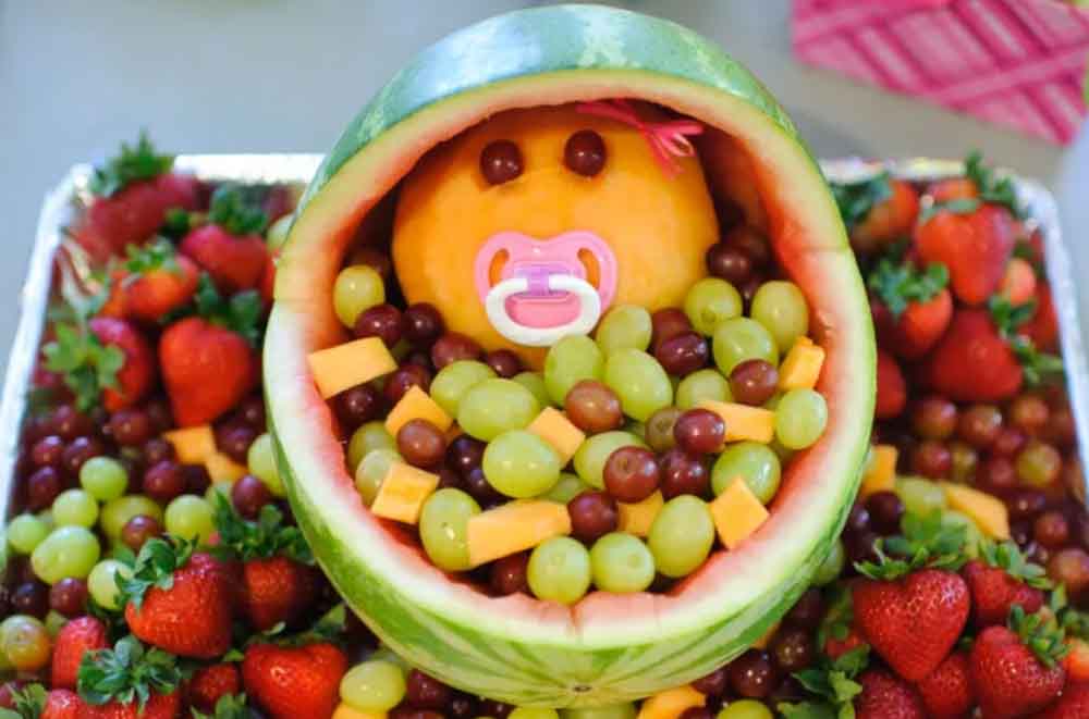 Watermelon carved into a baby carriage and filled with grapes, strawberries, and melon, a creative baby shower fruit centerpiece.