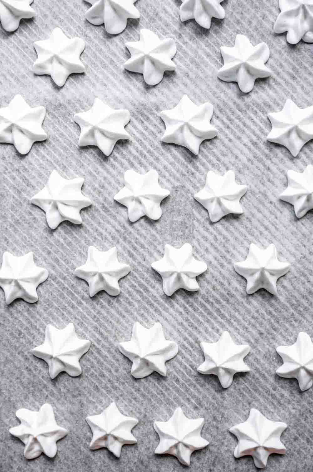 Rows of mini white meringue cookies piped into star shapes on a baking sheet.