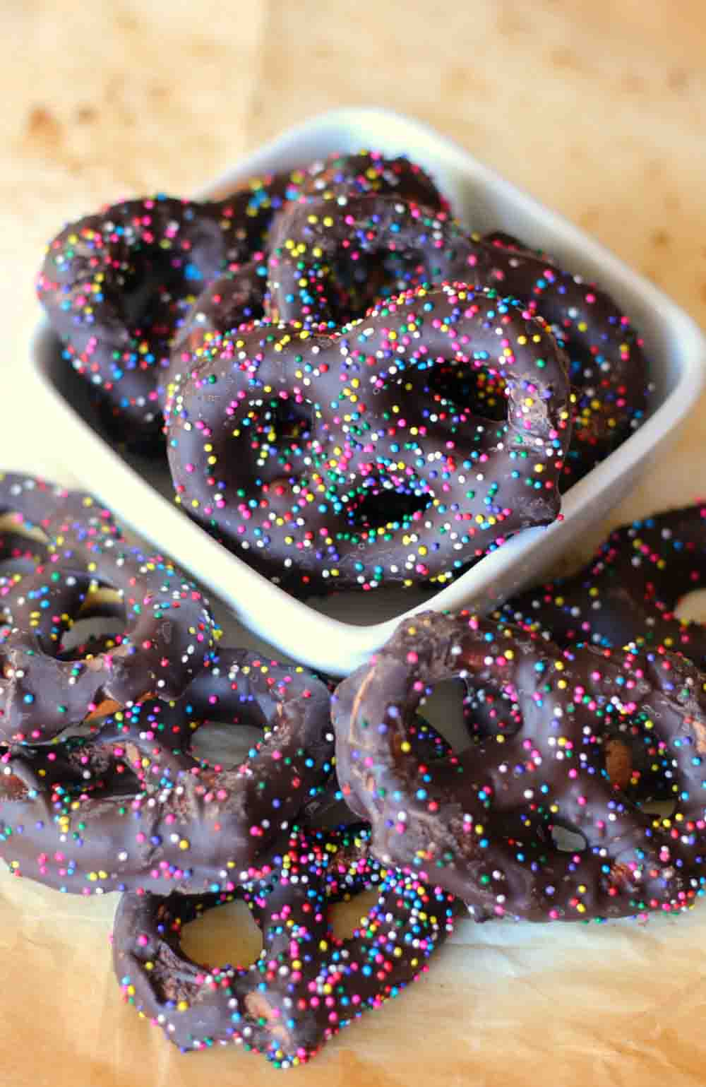 Chocolate-covered pretzels topped with colorful sprinkles in a small white dish.