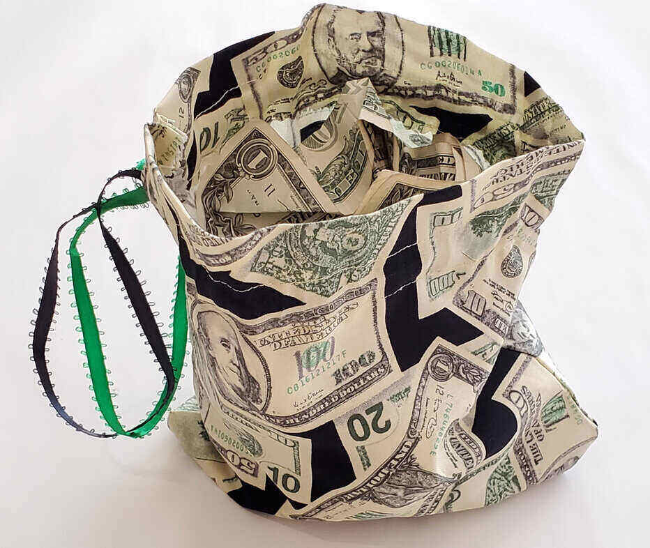 slouchy bag with green and black drawstring that has a fake money design all over it