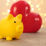 picture of a yellow piggy bank in front of a red heart with sparkle lights in the background