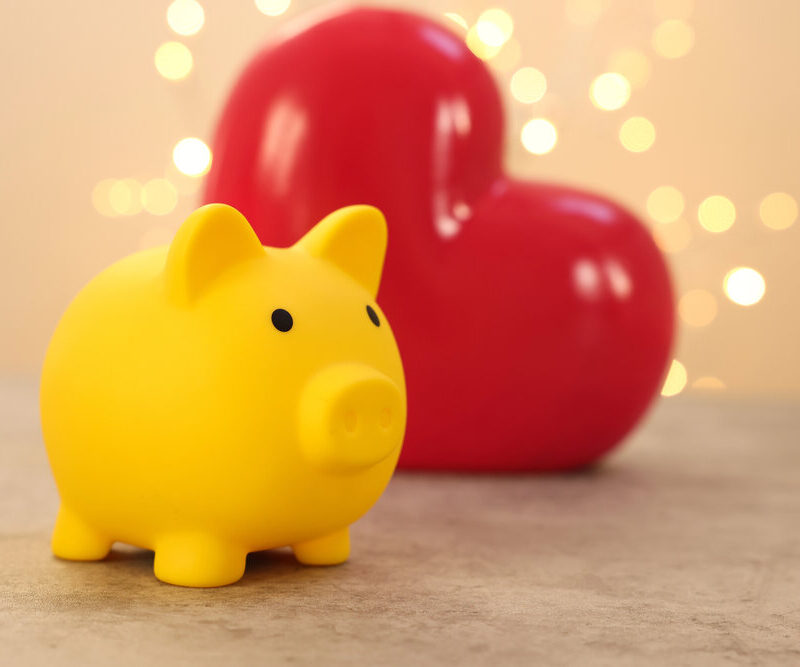 picture of a yellow piggy bank in front of a red heart with sparkle lights in the background