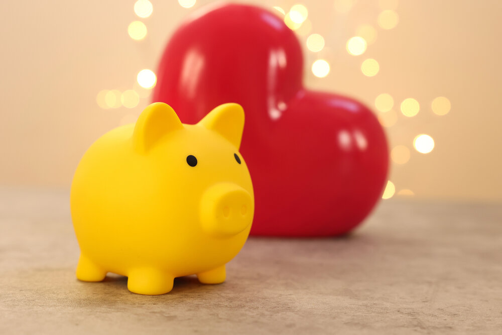 picture of a yellow piggy bank in front of a red heart with sparkle lights in the background