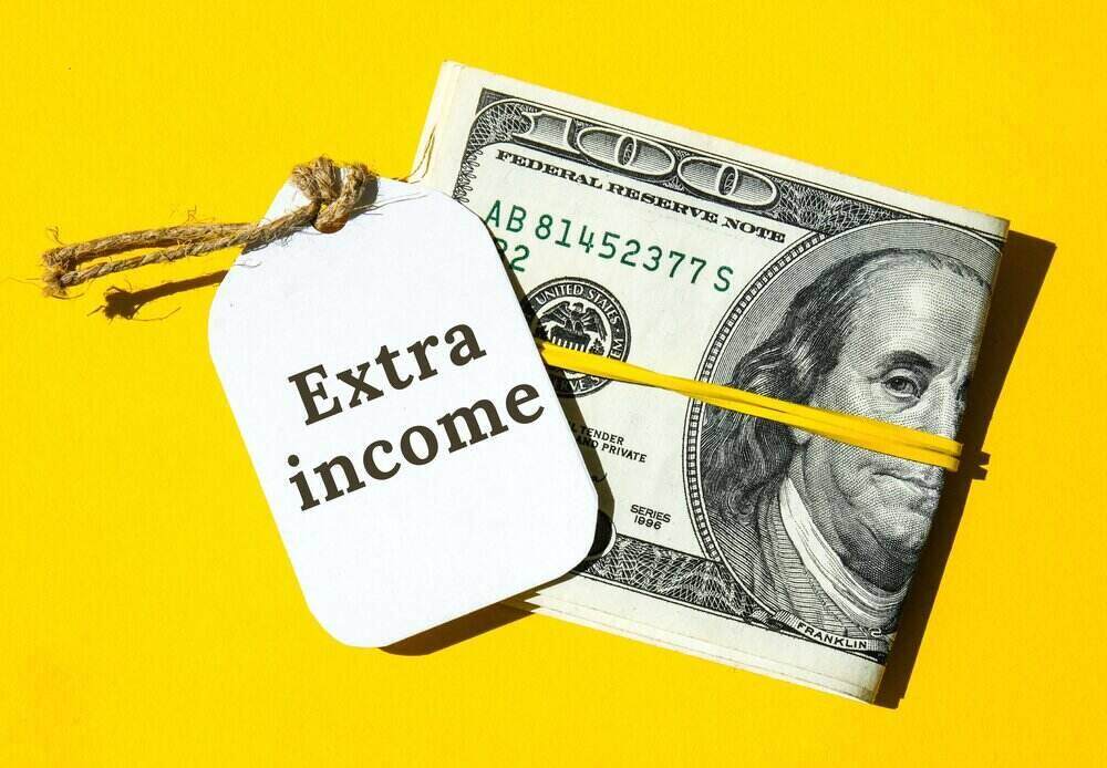 roll of 100 dollar bills with a tag that says extra income next to it on a yellow background